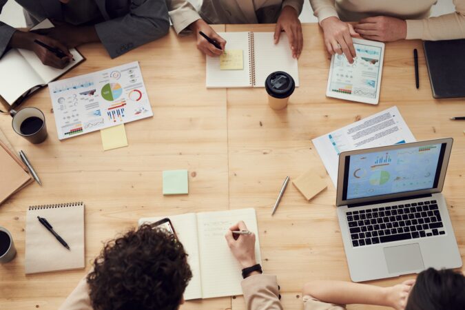 People sitting at a conference table with laptops, Post-it notes, and notepads