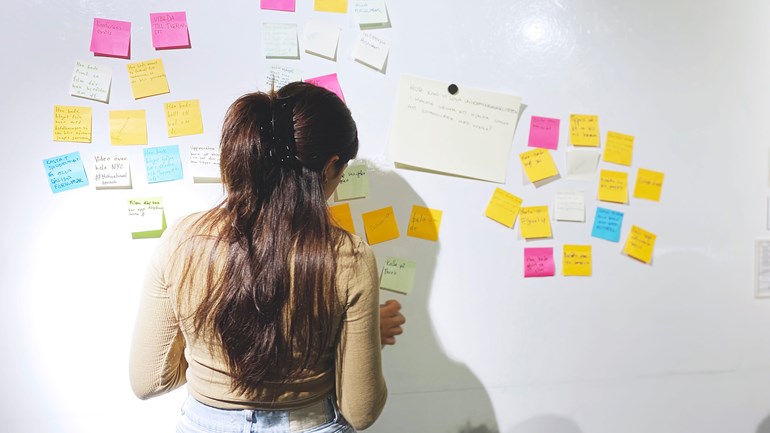 Praktikant som sätter upp post-it lapp under workshop om socialt entreprenörskap.